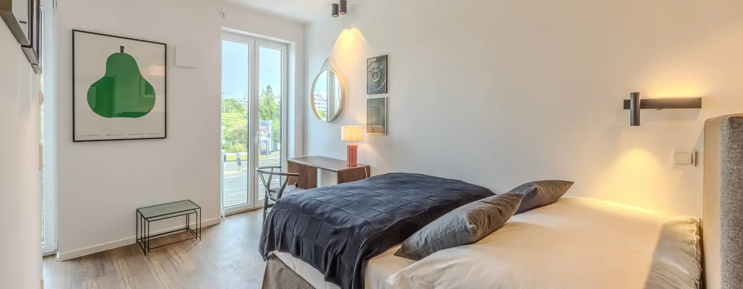 Großzügiges Schlafzimmer mit Balkontür und Arbeitsbereich in einem vollständig möblierten Studio M Apartment