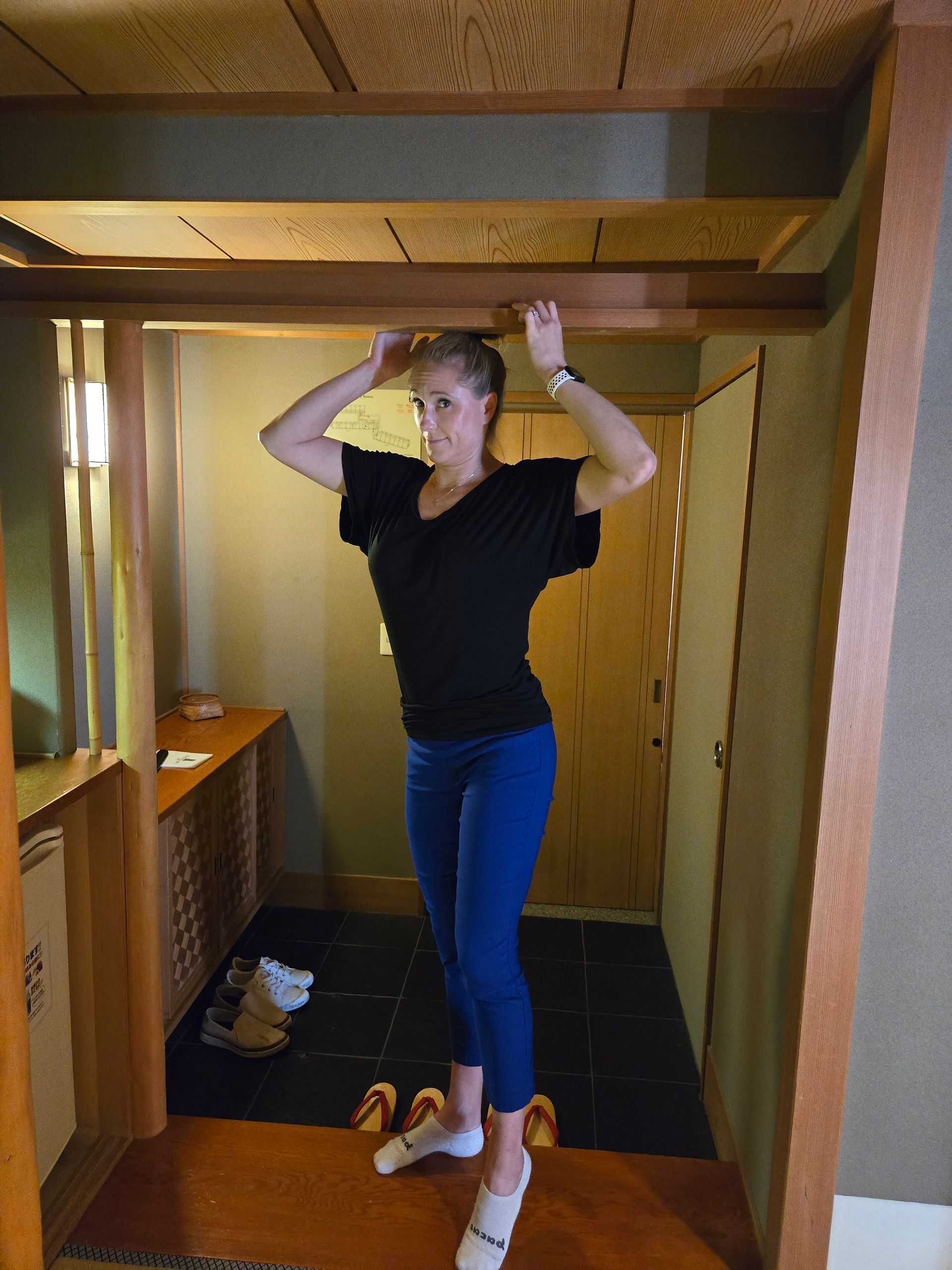 Tall traveler ducking under a low wooden doorway inside a traditional Japanese ryokan room at Nishimuraya Hotel Shogetsutei in Kinosaki Onsen.
