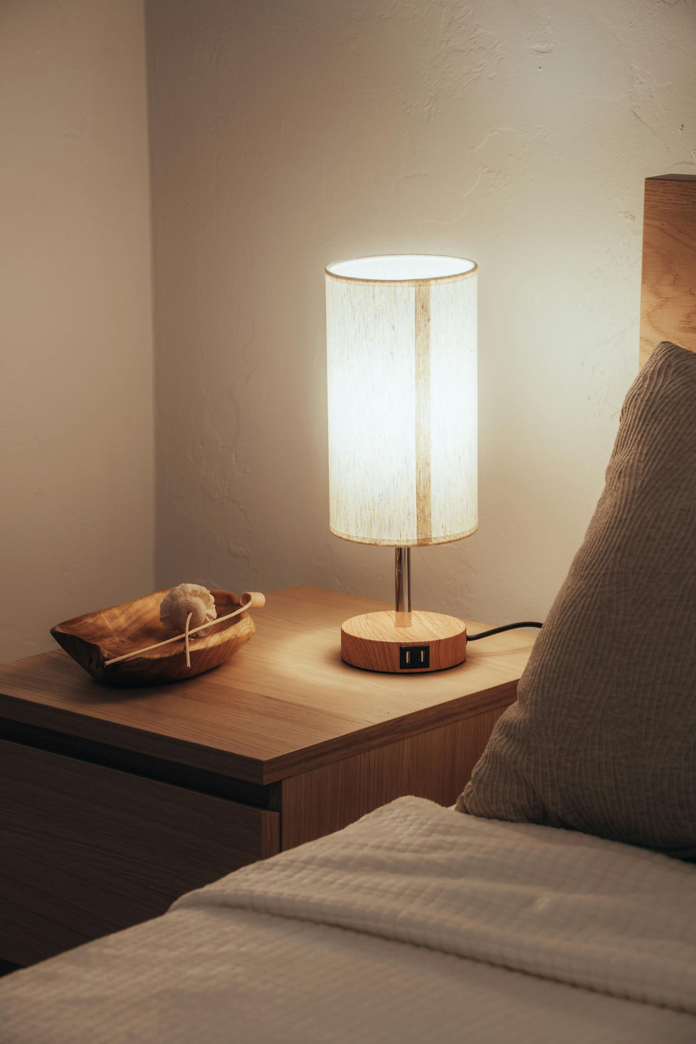 Bedside lamp glowing softly in dark room for a cool, restful sleep environment.