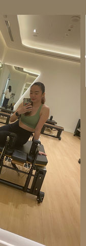 Woman with a green top sitting on top of a Reformer Pilates machine inside of OX Fitness