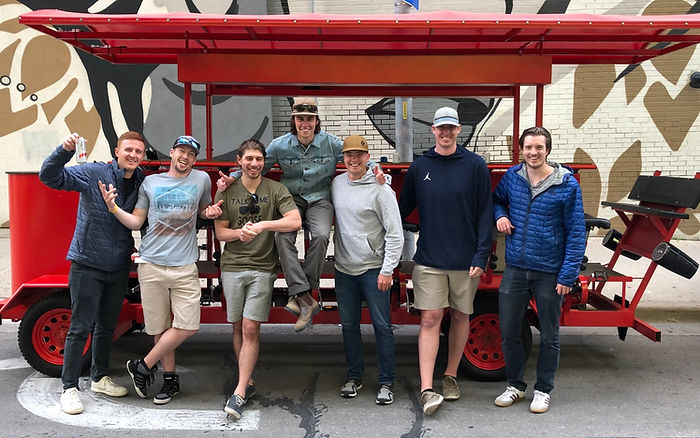 Excited bachelorette party crew gathered in front of a vibrant pedal-powered bike on 6th Street.