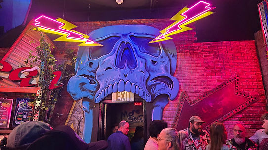 Visitors assemble beneath a vibrantly colored, skull-themed entrance at Universal Halloween Horror Nights 33, featuring neon lightning bolts and a spooky atmosphere.