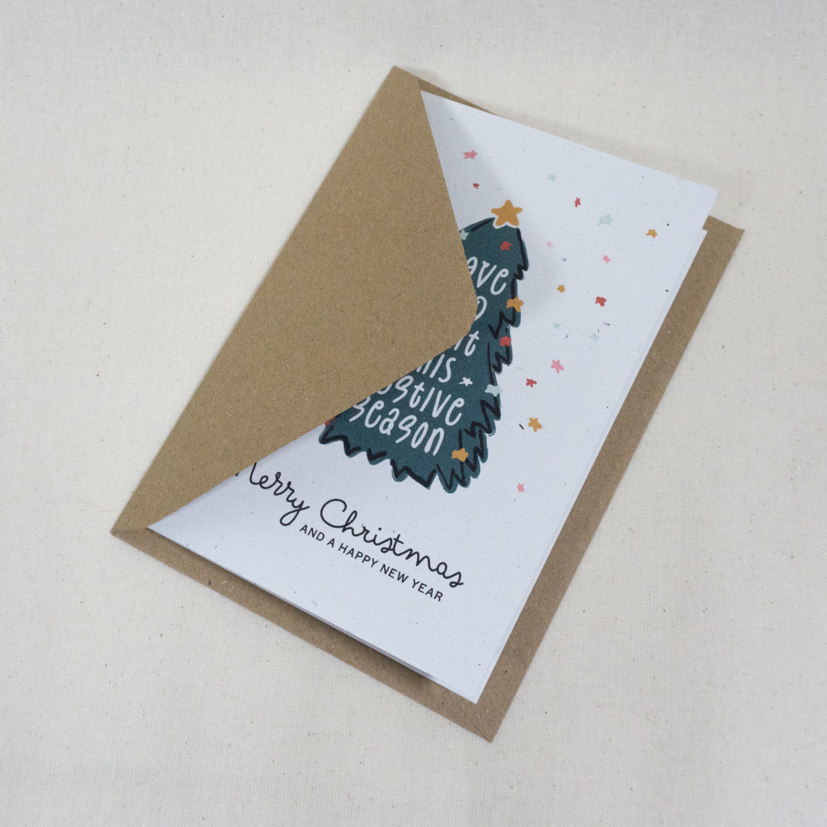 Christmas card featuring hand-drawn evergreen tree with text Love and Light This Festive Season with kraft brown envelope
