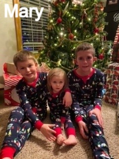 Three children in matching pajamas, Christmas tree in the background.