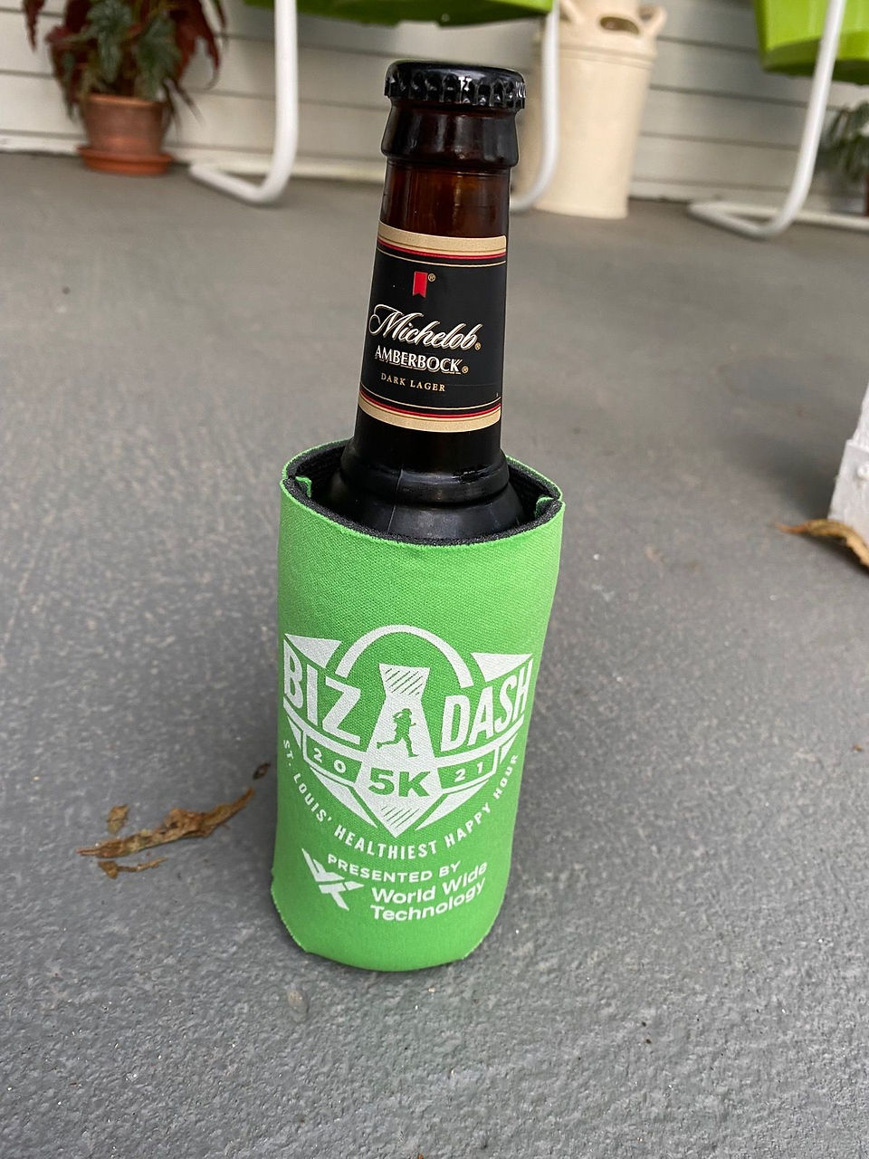 Beer bottle in green Biz A Dash 5K Koozie on concrete surface