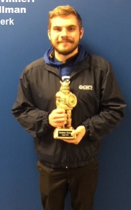 Man holding trophy with text, smiling, wearing jacket, standing in front of blue backdrop.