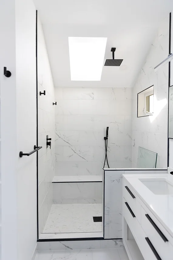 A skylit bathroom with a shower and a vanity