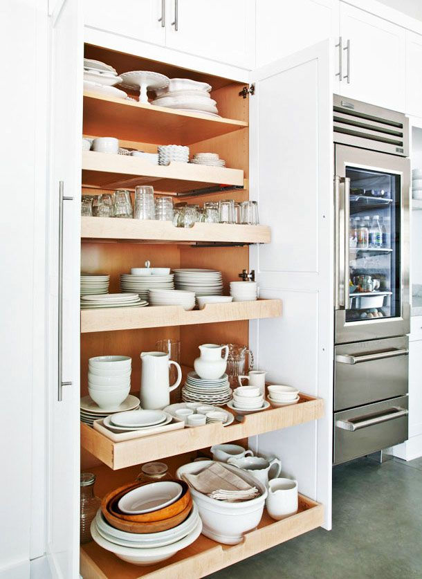 Pull out kitchen shelving inside of a cabinet with dish ware on each shelf.
