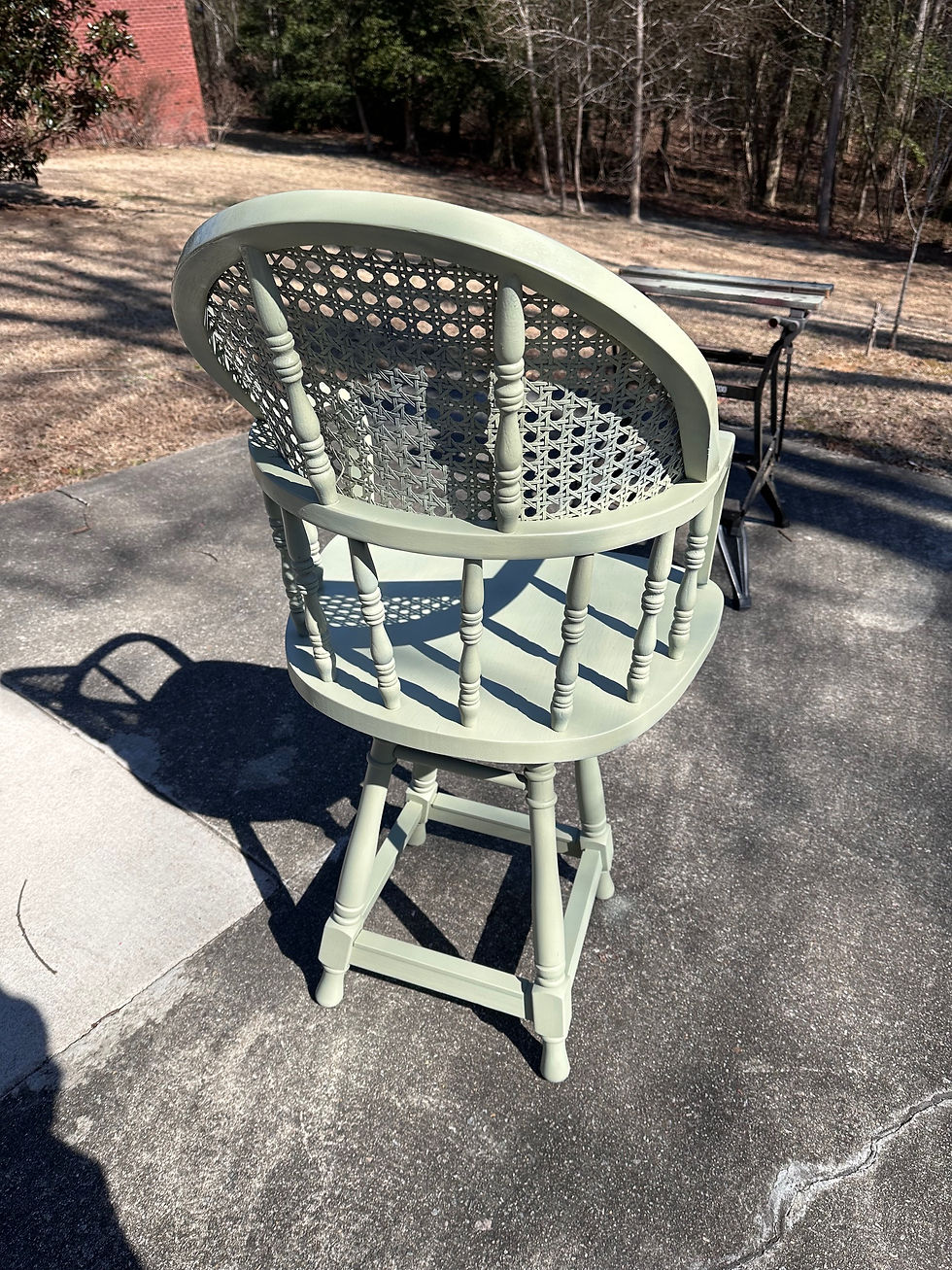 The same barstool as before, but it stands on a concrete pad, completely painted Rust-Oleum's Chalked Tate Green, from the back view.