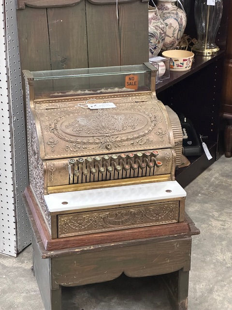 A gold and marble cash register which is highly, highly ornamented and detailled. It takes US dollars and coins, and is from the 1800s.