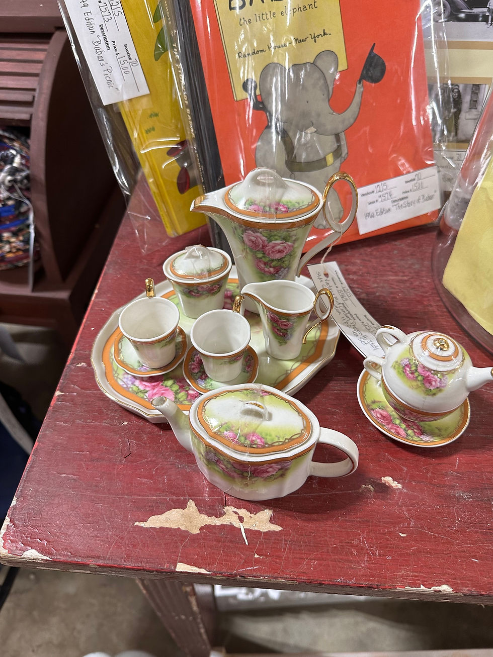 A complete child's tea set in the colors of pink, orange, green, purple, and cream. There are roses and various flowers with gilded details.