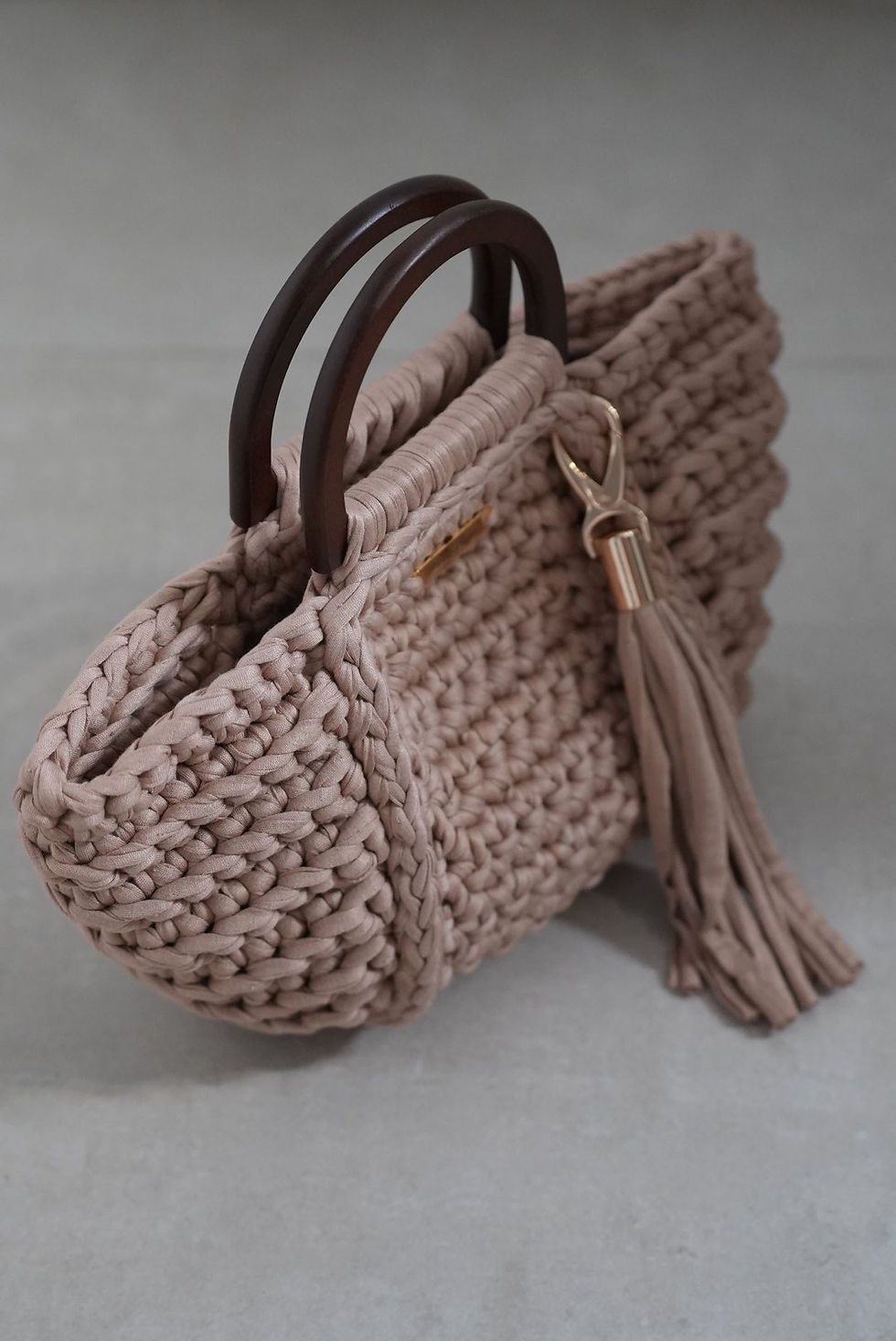 Solea Beige crochet tote in textured trapillo yarn with dark brown D-shaped wood handles and tassel detail.