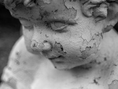 Weathered close-up of a sculpted child’s face with a cracked, textured surface.