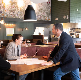 Three professionals collaborating in a Founding Farmers restaurant booth, discussing ideas and solutions during a work meeting.