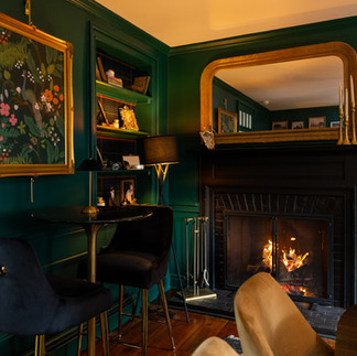 Intimate emerald green bar room with lit fireplace, gold-framed mirror, and velvet seating inside the Willowood Washington historic farmhouse