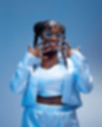 Zakisha Brown standing confidently in a futuristic light blue outfit with braids and tinted glasses, set against a soft blue 