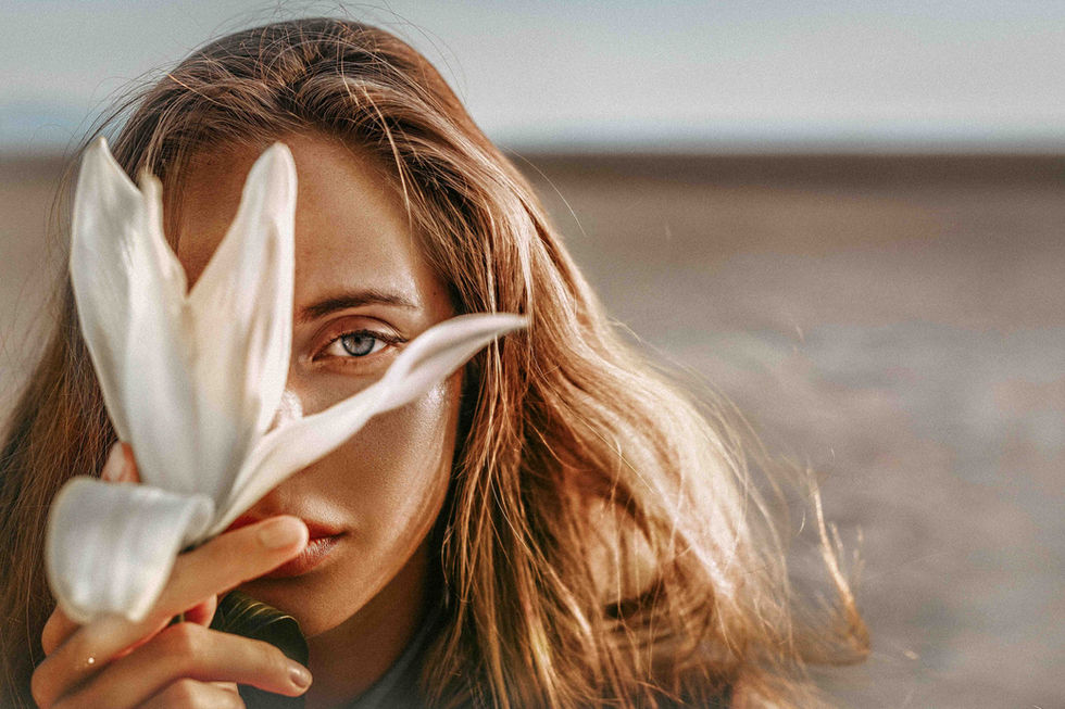Frau mit langen Haaren, hält eine weiße Blume vor ihr Gesicht, natürlicher Hintergrund, verträumter Ausdruck