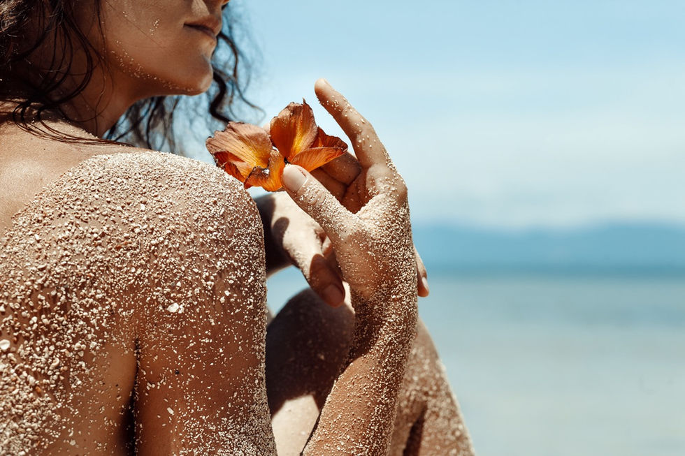 Mit Sand bedeckte Haut, Frau hält eine orangefarbene Blume, Meer im Hintergrund, entspannte Strandatmosphäre