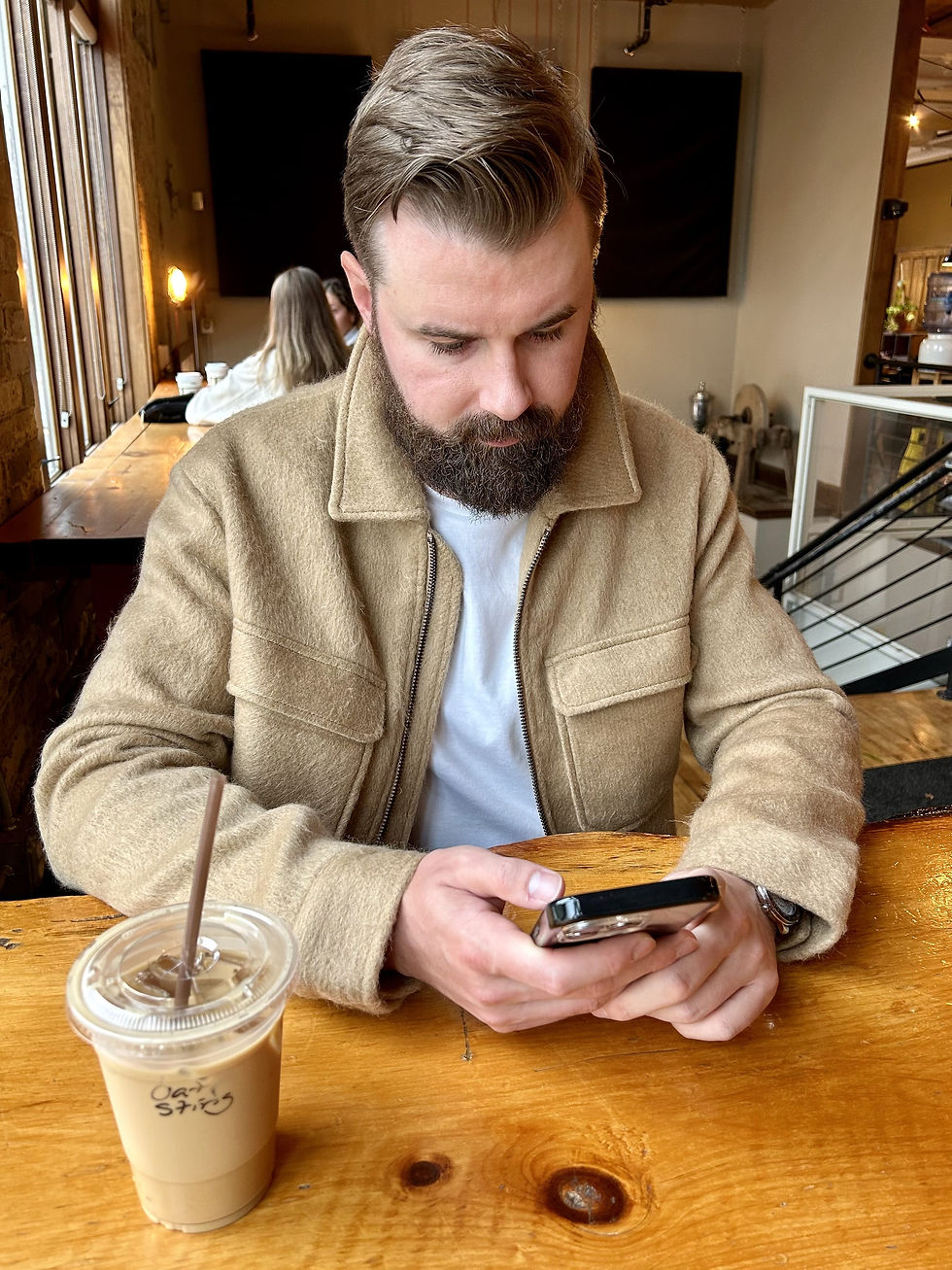 Christopher Csiszar sitting in a cafe looking at his cell phone with an oat milk latte on the table