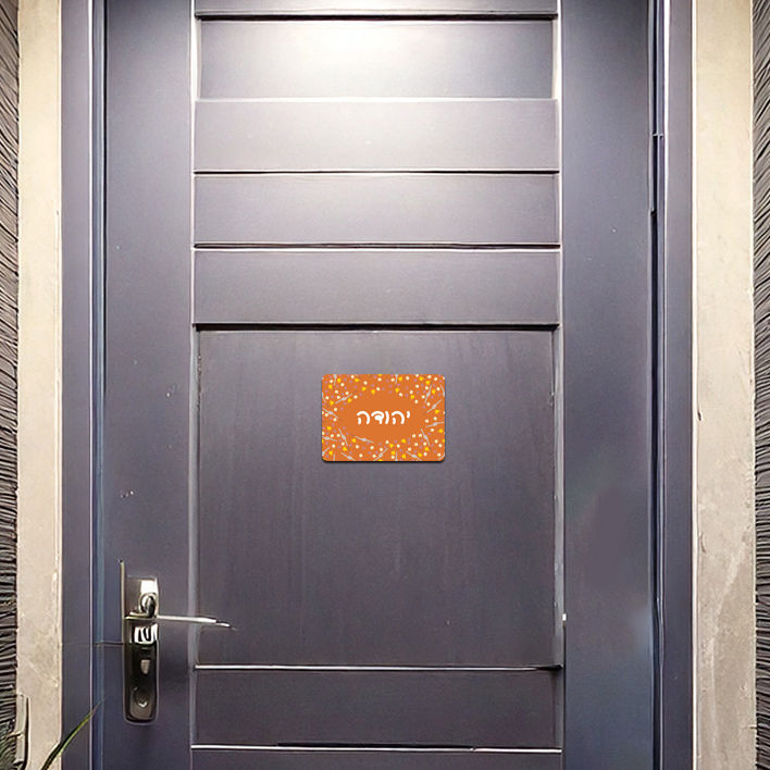 תמונה ממוזערת: שלט מגנט לדלת כניסה על רקע דלת מתכת אפור כהה. השלט מעוצב עם פרחי חלמונית ונרקיס ומציג שם בהתאמה אישית