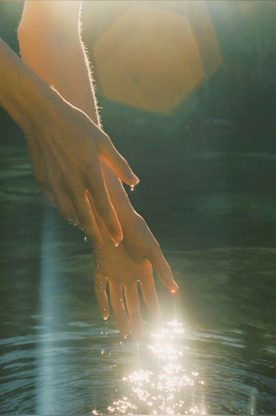 Hands reaching for water, a drop symbolizing the connection to a vital life force.