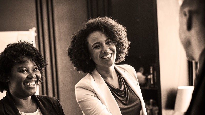 Two women smiling as one of them shakes hands with a man