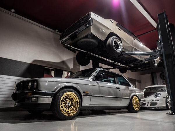 ガレージでリフトアップされた旧車と金色のホイールのBMW E30