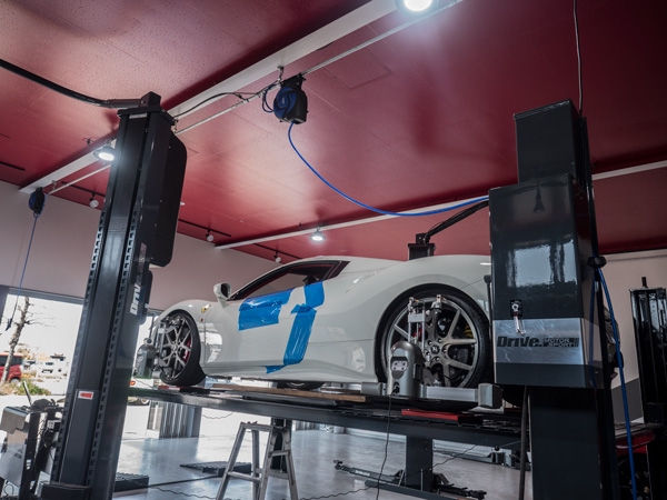 整備工場のリフトでアライメント調整中の白いスポーツカー