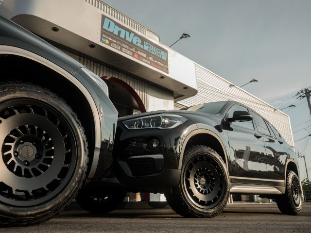 Drive. MOTOR SPORTの前に並ぶ黒いBMW X1とカスタムホイール