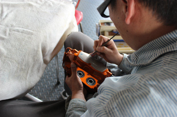 オレンジ色のブレーキキャリパーに筆で色を塗る作業員