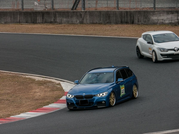 サーキットのコーナーを走る青い車両と白いSUV