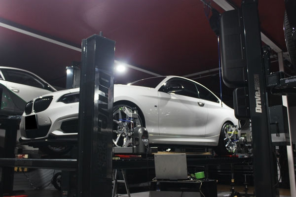 整備工場のリフトでアライメント調整中の白いBMW M2