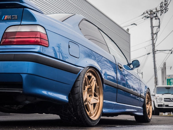 ブロンズのホイールを履いた青いBMW M3 E36のリアビュー