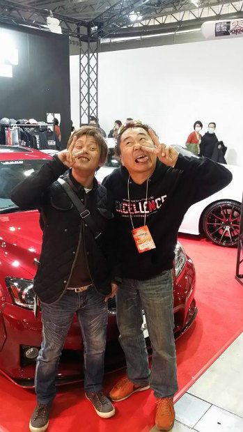 展示会の赤い車の前でピースサインをする男性二人