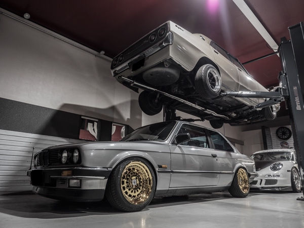 ガレージでリフトアップされた車と金色のホイールのBMW E30