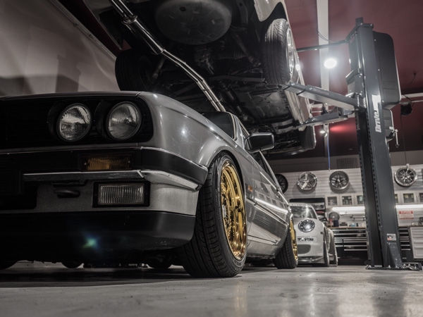 リフトアップされた車と金色のホイールを履いたクラシックカーのあるガレージ