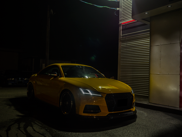 夜間の店舗前に停車した黄色いアウディTT