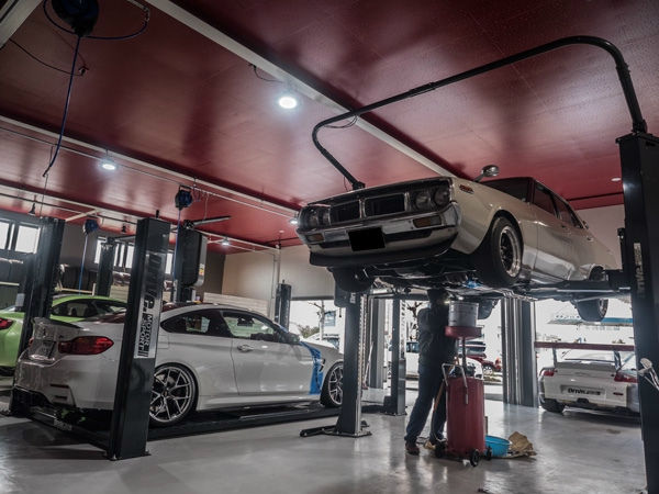 リフトアップされた旧車と整備中のスタッフがいるガレージ