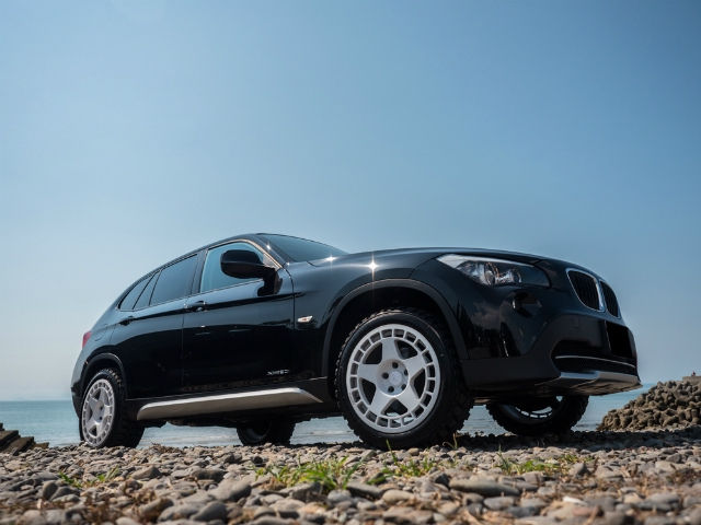 海岸の小石の上に停車する、白いホイールを履いた黒のBMW X1