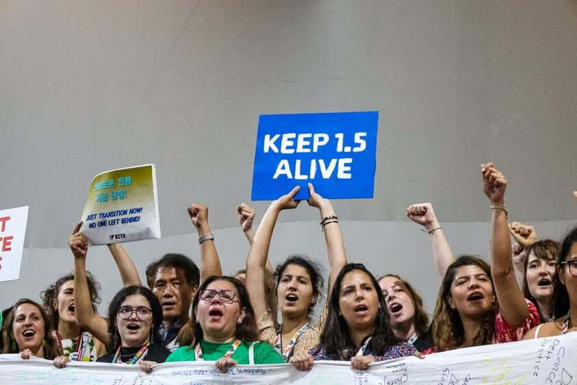 Climate justice advocates take action, holding signs for just transition and upholding the 1.5°C guardrail during an action in the Blue Zone of COP30 in Belém, Brazil. Photo Credit: Katherine Quaid / WECAN