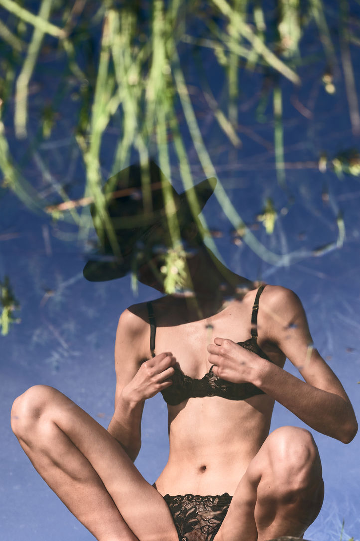 a reflection of a girl in the water sitting on the rock in black lingerie