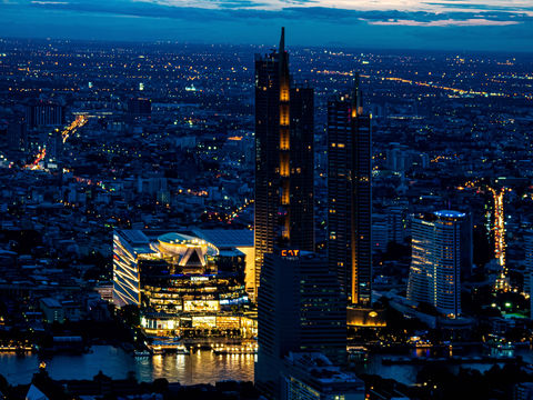 A professional blue-hour photograph of the vast Bangkok skyline from above, with the brightly illuminated Icon Siam mall creating a focal point on the river, showcasing a stunning cityscape.
