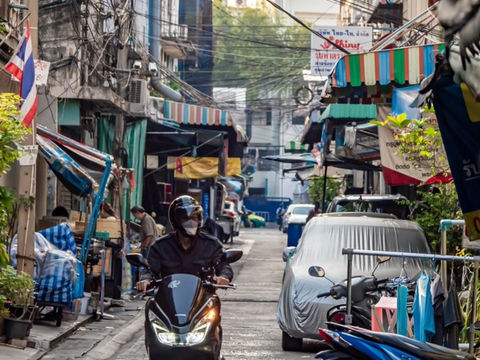 Local rider navigating a scooter down a quiet residential alleyway in Bangkok
