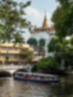 The Golden Mount temple (Wat Saket) in Bangkok, framed perfectly by a rustic bridge and green foliage from across a canal.