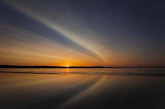 Colourful Sunrise – orange sun and sweeping clouds reflected across calm water, photographed by Chris Baguley