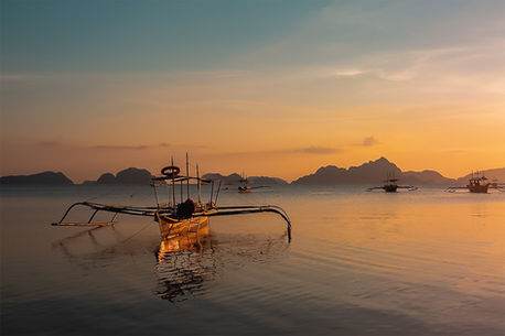 Anchored in Gold – traditional outrigger fishing boat on calm water at sunset in the Philippines