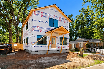 Two-story home under construction in Greenville, SC, featuring exterior house wrap, framed front porch, and ongoing site preparation.