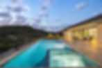 Modern home with illuminated pool and hot tub, hills at dusk