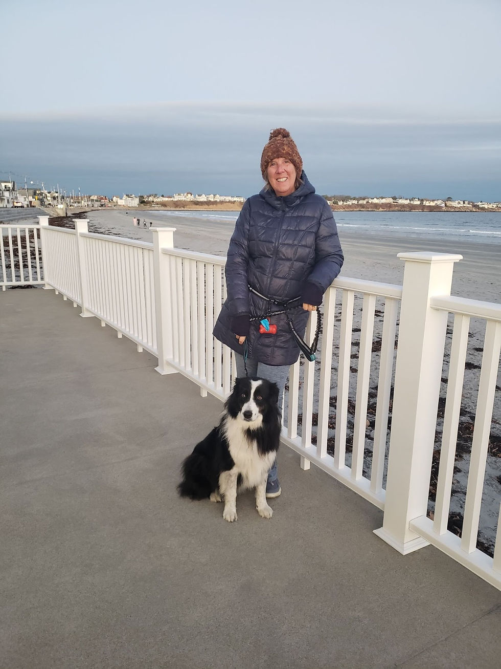 Brenda standing on a boardwalk near the ocean with her dog on a cold day