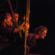 Dancers dressed as poor Londoners peer out from a scaffolding structure